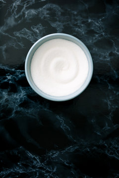 White sugar in blue bowl on black marble