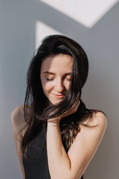Dreamy portrait of attractive brunette with closed eyes and tender smile in contrast sunlight