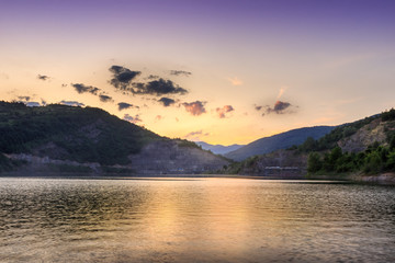 Perfect golden hour over reflective lake and horizon rocky mountains with colorful sky and fluffy clouds