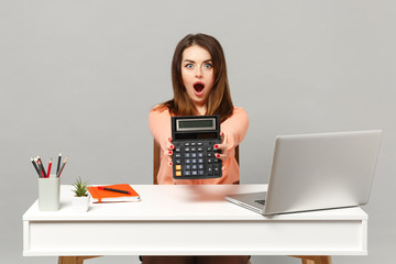 Young shocked woman in pastel clothes keeping mouth open, hold calculator, work at desk with pc laptop isolated on gray background. Achievement business career lifestyle concept. Mock up copy space.