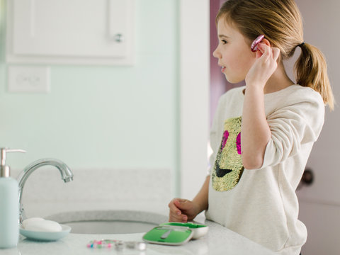 Young girl putting her hearing aids on