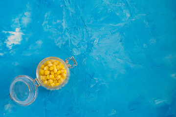 Fototapeta na wymiar Canned marinated pickled fermented sweet corn in a glass jar on blue white concrete background with copy space