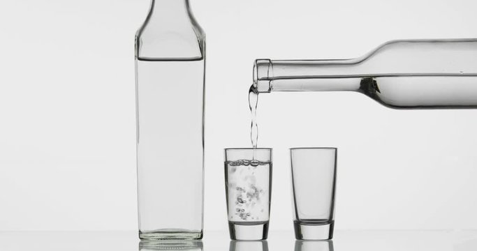 Pouring up two shot of vodka from a bottle into glass. White background
