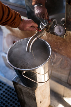 Old rugged maple syrup farmer adjusts valve as fresh hot maple syrup is finished