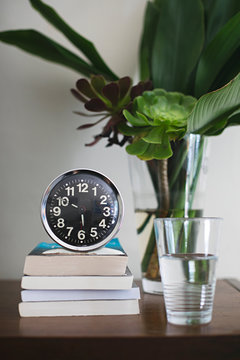 Bedside table with vintage analogue alarm clock, books, water and vase