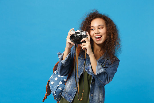 Young african american girl teen student in denim clothes backpack hold camera isolated on blue wall background studio portrait. Education in high school university college concept. Mock up copy space