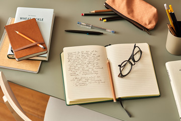 Notebook with handwritten text, pencil and glasses on desk.