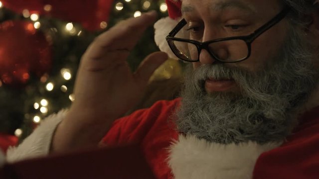 close up of Santa reading in front of Christmas tree