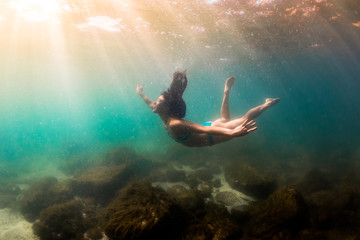 Woman gracefully moving underwater in sunlight dappled lake