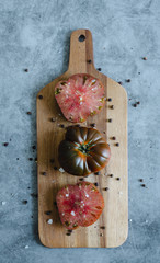 Sweet Marmande tomatoes whole and cut on wooden board and stone background.