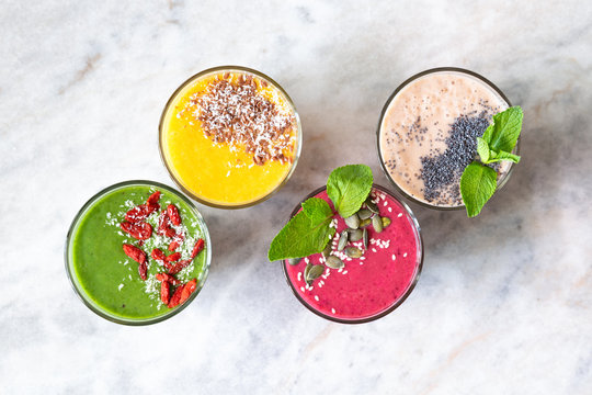 Healthy vegan smoothies with forest fruits, bananas, spinach, coconut milk, pineapple, kiwi, mint, turmeric, chia, flax seeds, goji berry, and coconut flakes