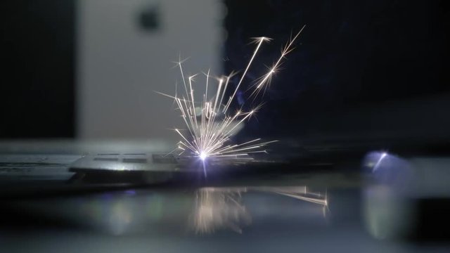Industrial laser cutter with sparks. The programmed robot head cuts with the aid of a huge sheet of metal temperature. Close up.