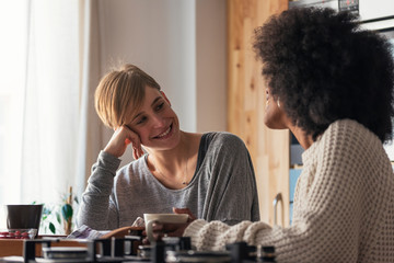 Two beautiful girls chatting while having breakfast in the kithen at home.