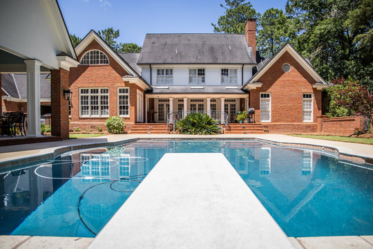 Large Blue Swimming Pool Outdoors with Brick Pool House and Home with pool Cleaner running
