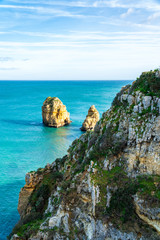 Cliffs with vegetation and rocks in the ocean at the coast of Lagos, Portugal