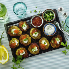 Russian traditional potato pancakes served with red caviar, green onions and sour cream on a tray with white wine and lemon
