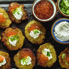Russian traditional potato pancakes served with red caviar, green onions and sour cream on a tray with white wine and lemon