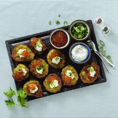 Russian traditional potato pancakes served with red caviar, green onions and sour cream on a tray with white wine and lemon