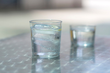 Glass of water with ice on a metallic table outdoors in a sunny day