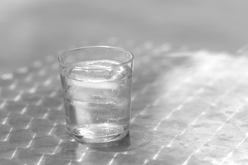 Glass of water with ice on a metallic table outdoors in a sunny day