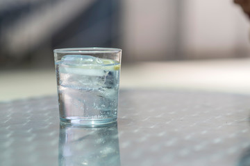 Glass of water with ice on a metallic table outdoors in a sunny day