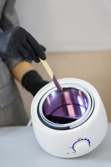 Fototapeta na wymiar Eyebrow waxing. Hot wax of lilac color of a liquid consistence. Wax heater