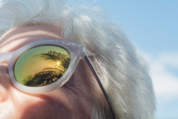 Senior woman with palm trees reflected in sunglasses
