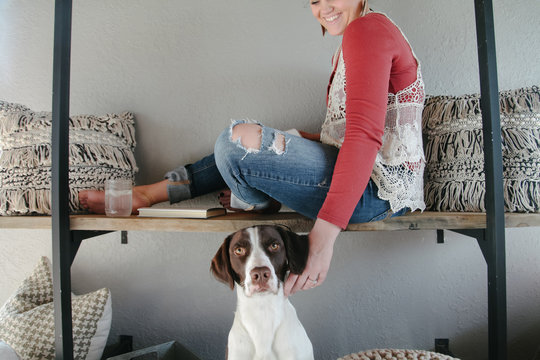 woman reaches down to pet dog while she sits leisurely on bench reading