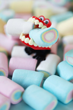 Many multi colored candies and dracula chattering teeth chewing two marshmallows
