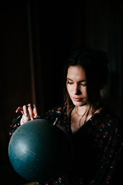 portrait of a beautiful young brunette with light eyes in a dark room with a  constellation world globe