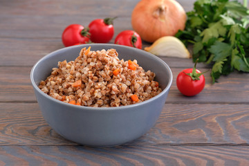 buckwheat  porridge with carrots and parsley in plate. On background of Golden onions and green parsley.
