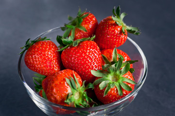fresh delicious strawberries in a transparent bowl on a dark gray background, close-up