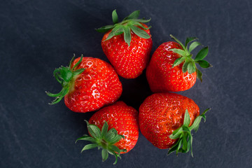 five fresh strawberries laid out in a circle on a dark gray background