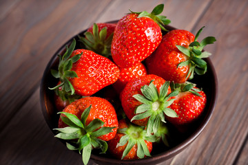 fresh ripe strawberries in a brown bowl on a brown wooden background close-up