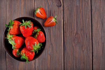 fresh ripe strawberries in a brown bowl on a brown wooden background top view, copy space