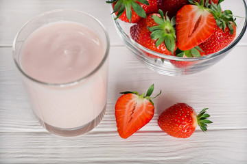fresh strawberries in a transparent bowl and a glass of yogurt or cocktail on a white table