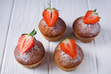 four cupcakes with strawberries on a white wooden background