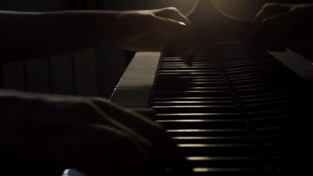 Woman pianist hands playing gentle classical music on a beautiful grand piano close-up in the sun rays. Piano keys close up in dark colors. Student trains to play the piano