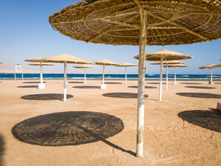 Image of straw umbrellas on the ocean beach at hot sunny day against blue sky