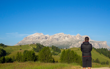 A person admires the fantastic Dolomites in Italy during the summer period. The massive Sella in the background. Hiker photographed from behind. Dolomites a Unesco World Heritage