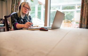 Woman listening to webinar on her laptop,wearing headphones