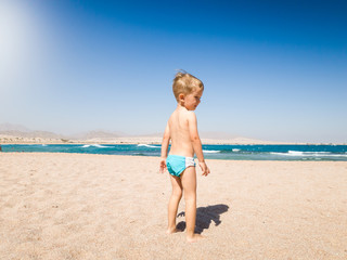 Image of adorable 3 years old little boy walking on the hot beach sand to the sea. Child relaxing and having good time during summer holiday vacation.