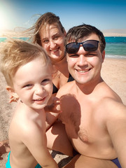 Fototapeta premium Selfie portrait of happy smiling mother, father and little son making selfie photo on sea beach. Family relaxing and having good time during summer holiday vacation.