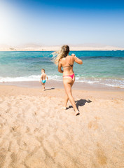 Fototapeta premium Image of young mother running to her little child walking in the sea. Caring parent preventing danger situation during beach holiday vacation.