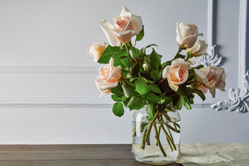 bouquet of light pink roses on a wall with plaster decorative elements, on a wooden table