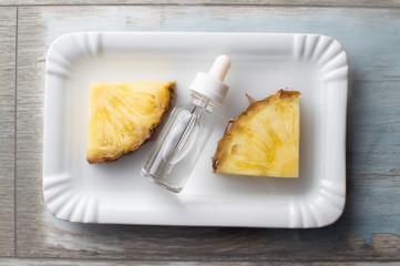 Pineapple flavored vape liquid lies on a white plate with two pieces of pineapple