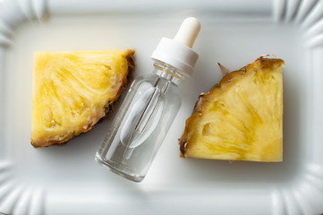 Pineapple flavored vape liquid lies on a white plate with two pieces of pineapple