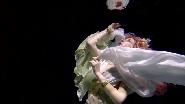 young sinking bride is stretching hand to water surface, her body is plunging inside sea