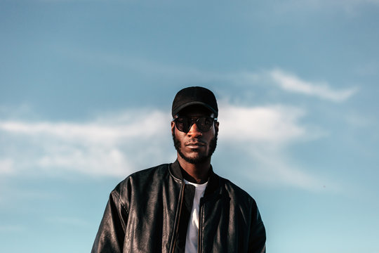 Young black man wearing black cap and sunglasses looking at came
