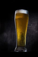 Cold beer glass with condensation and bubbles over grey concrete background
